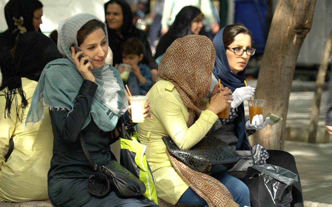 Foto von einer Gruppe junger iranischer Frauen mit Kopftuch, die ein Getränk in der Hand halten. Eine hält ein Handy ans Ohr.