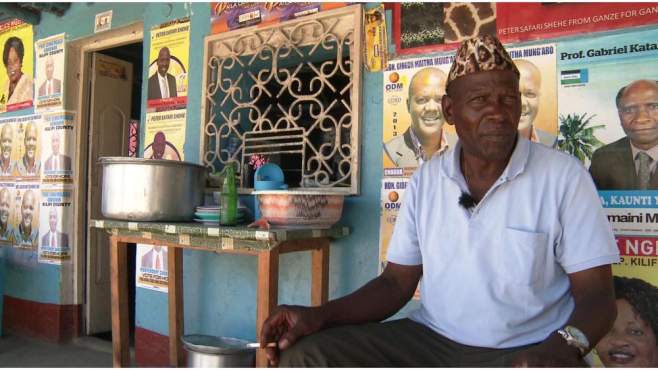 Afrikanischer Mann mit Fellmütze sitzt vor einem exotischen Laden